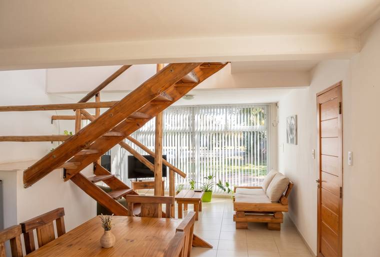 Living-comedor con escalera de madera, sillón y ventanal hacia el parque
